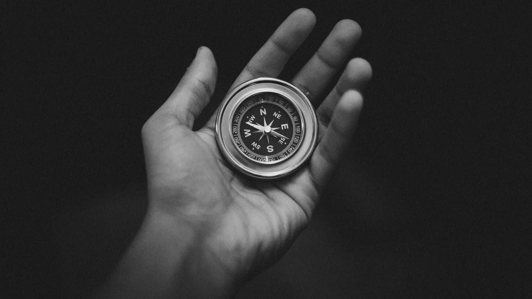 Hand holding an analog compass, black and white — a metaphor for finding direction