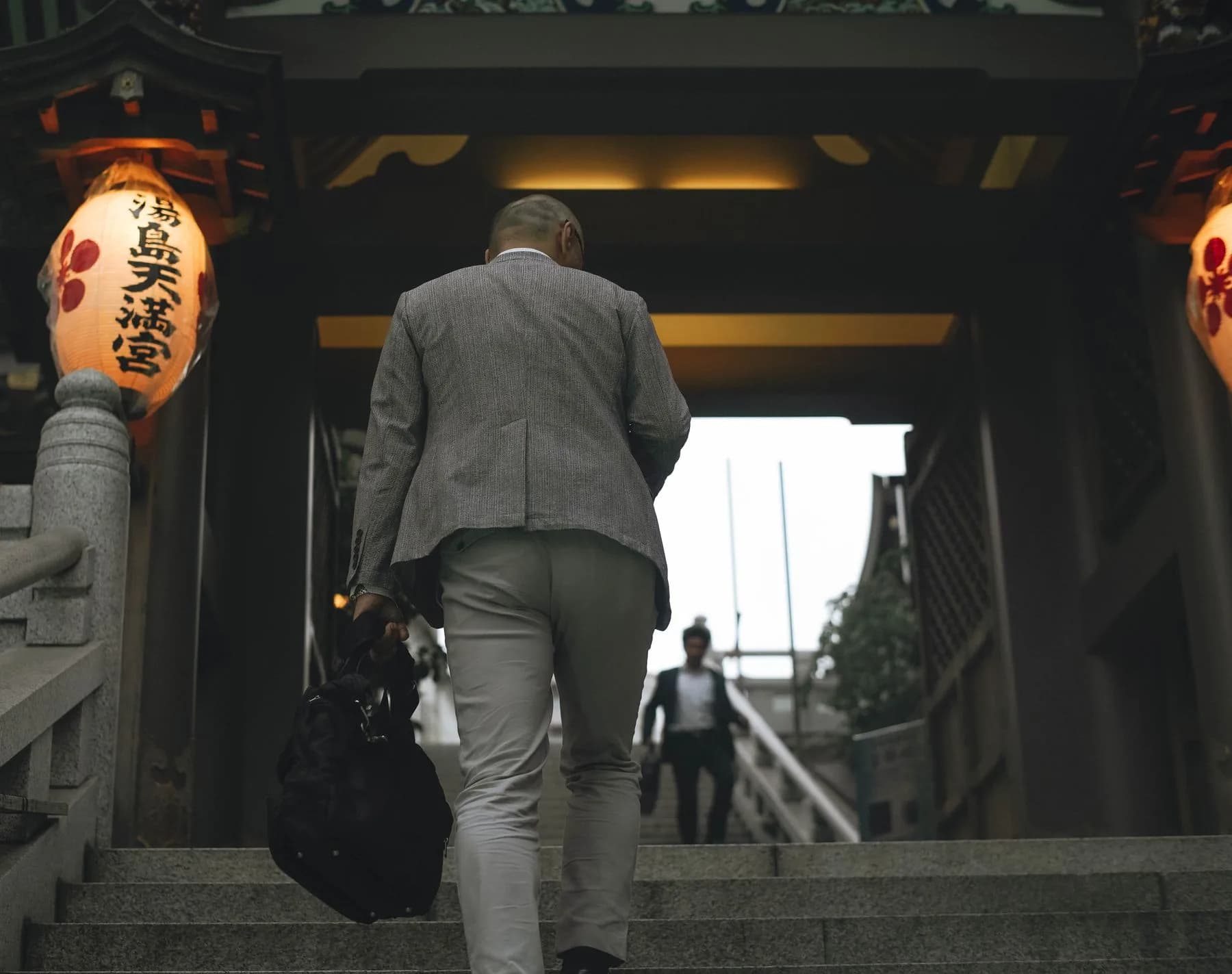 Businessman in formal attire ascending a staircase, seen from behind — representing professional transition and forward movement